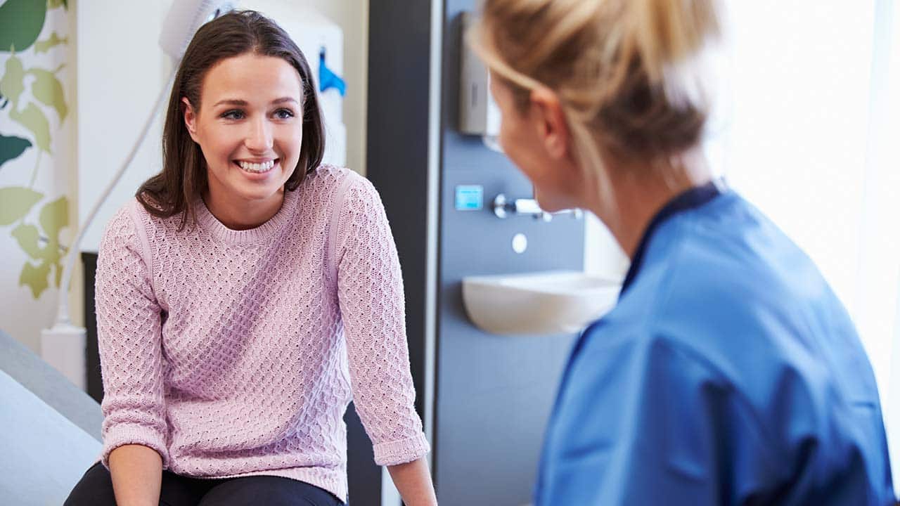 a client sites on an exam table talking with doctor about losing weight