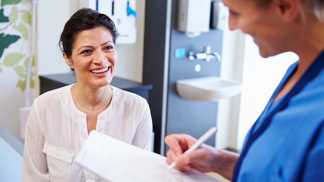 a woman is smiling while talking to a weight loss specialist who is taking notes on her medical history