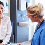 a female client is smiling while talking to a physician assistant who is wear blue scrubs a stethoscope is around her neck